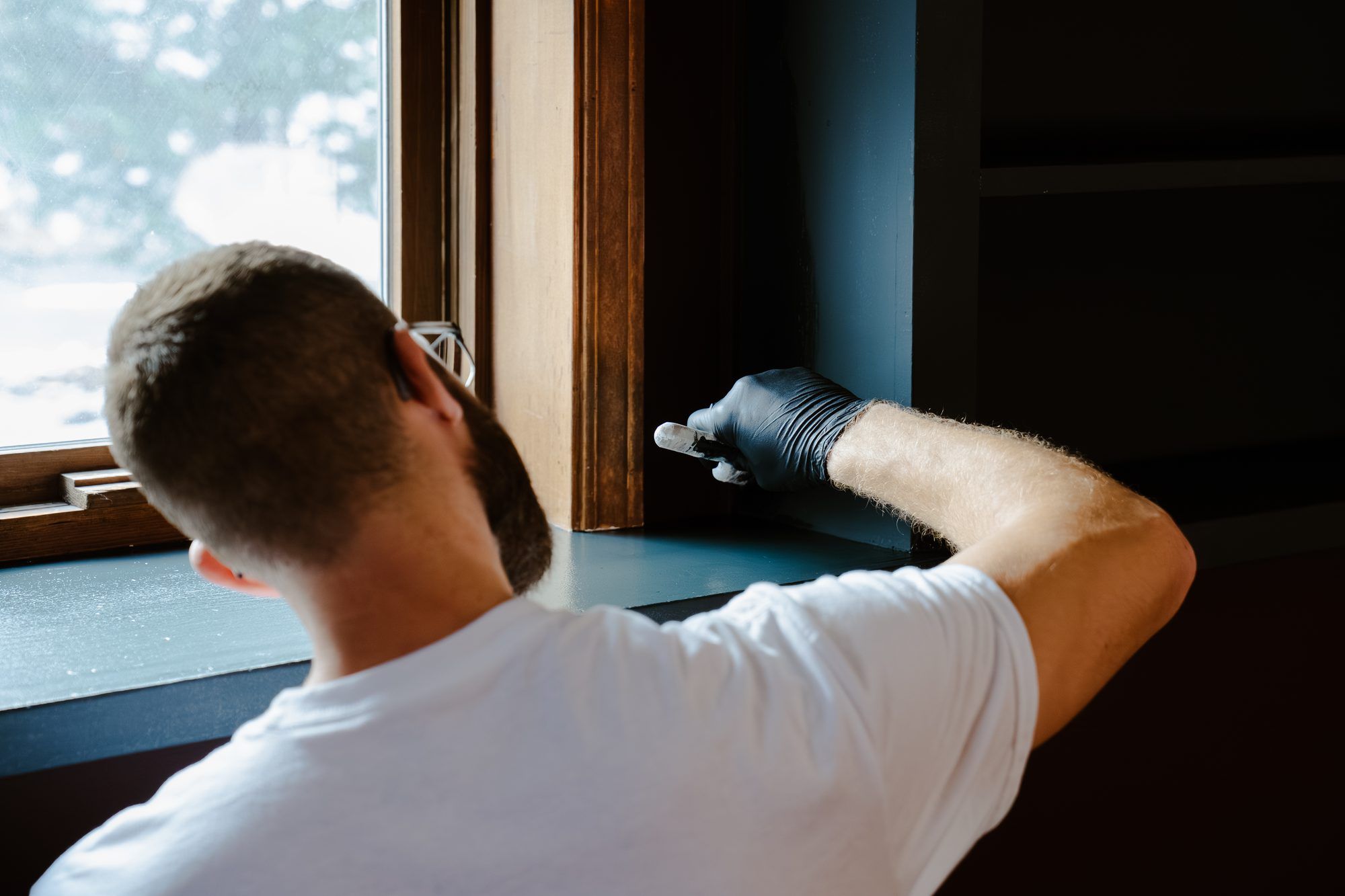 Ryan Lewis brushing window trim in a lived-in home